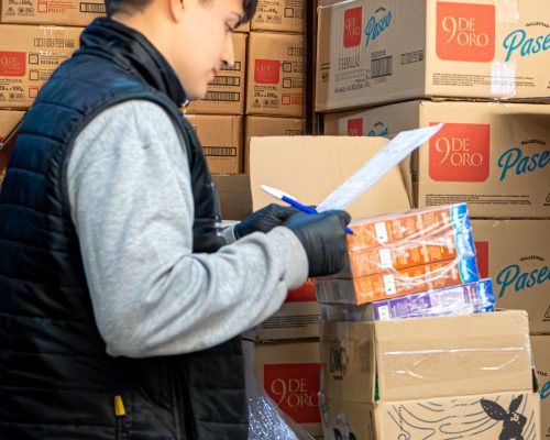 Empleado controlando stock de mercadería, con una caja de 9 de Oro y de Paseo